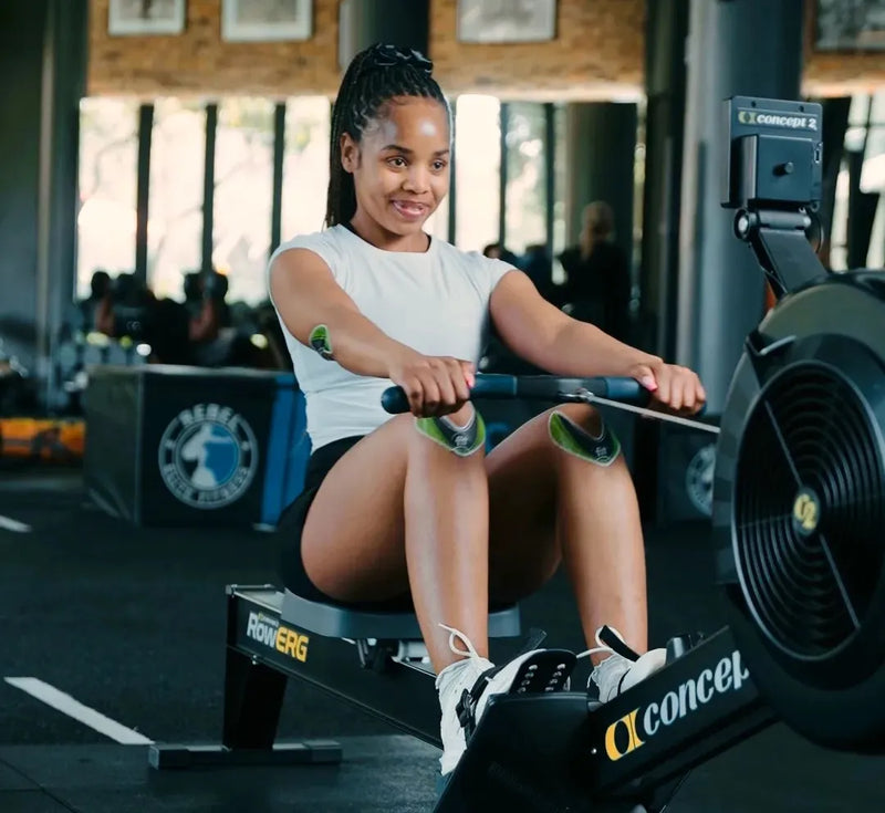 A woman rowing on a Conners Rowing machine in a gym setting.
