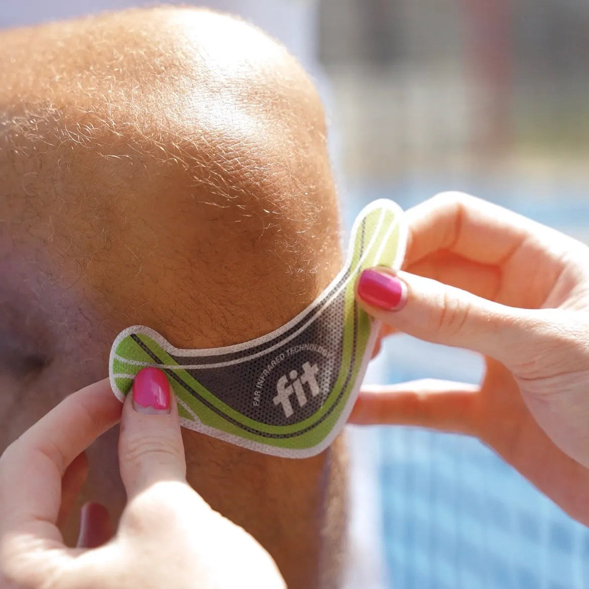 A close-up of a person applying a green and white FitPtach Therapy patch to another person's knee.